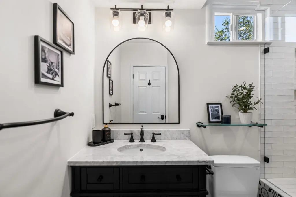 Modern bathroom with black vanity, marble counter, and arched mirror.