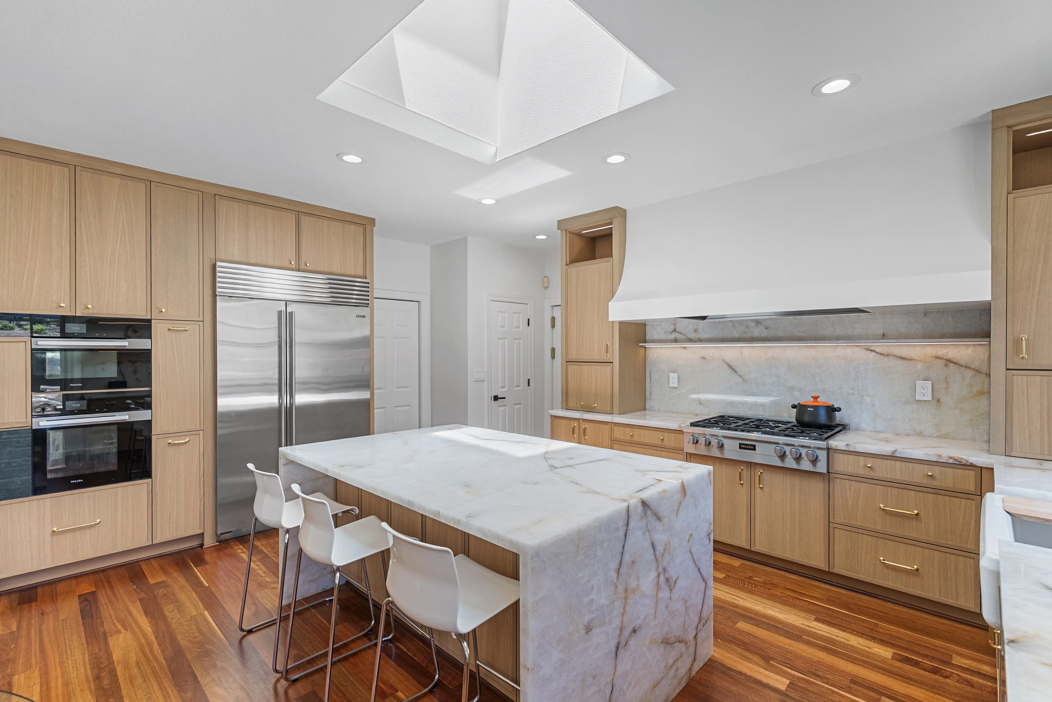 Modern kitchen with large marble island, stainless steel appliances, and wood cabinets