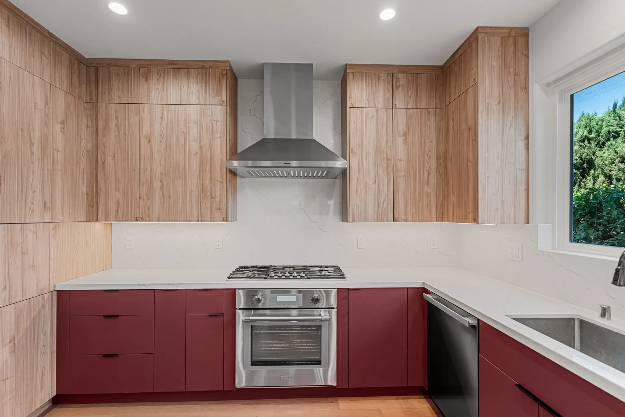 Modern kitchen with wood and red cabinets, stainless steel appliances, and white countertops.