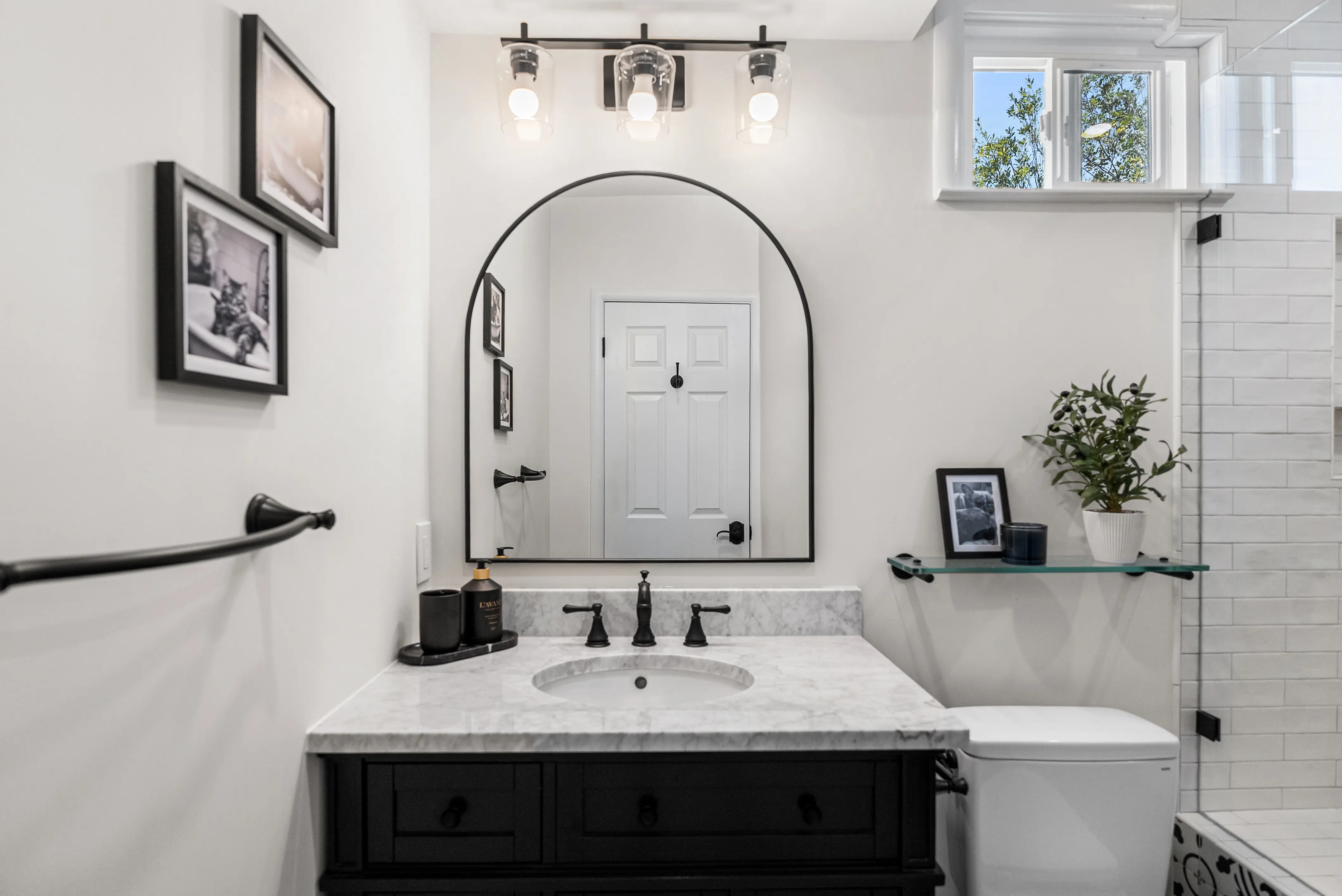 Modern bathroom with black vanity, marble counter, and arched mirror.